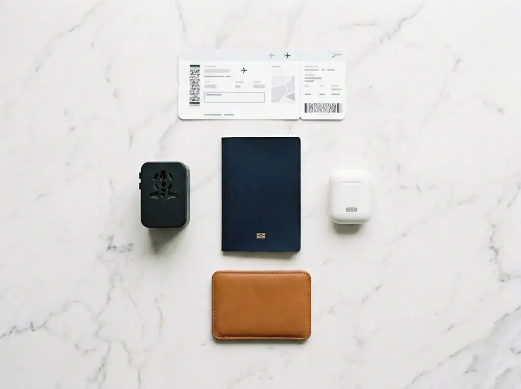 Travel essentials flat lay including passport, earbuds, boarding pass, and travel adapter